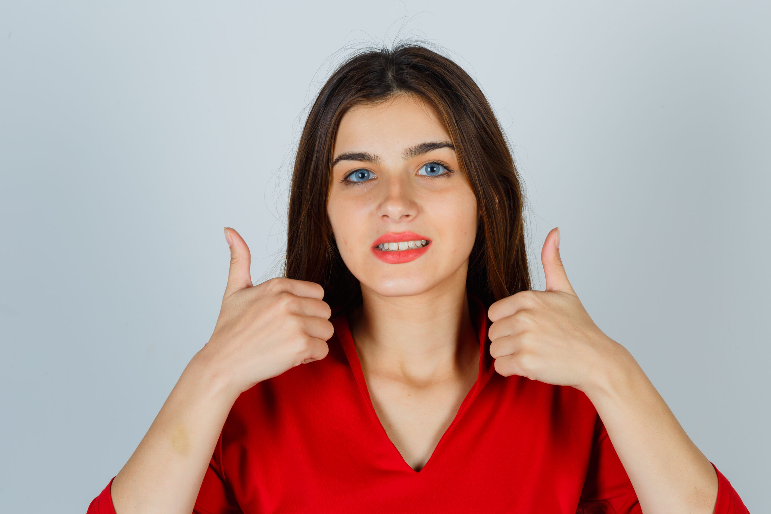 young lady in red blouse showing thumbs up and looking glad , front view. Emily